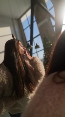 Evde, genç ve güzel bir kadın aynanın önünde Noel geyiği maskesi deniyor. Yüksek kalite 4k görüntü