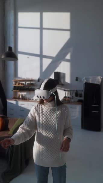 在一个光滑的现代公寓里 一位年轻的女士穿着浅色的衣服 戴着一副虚拟现实的耳机 高质量的4K镜头 — 图库视频影像