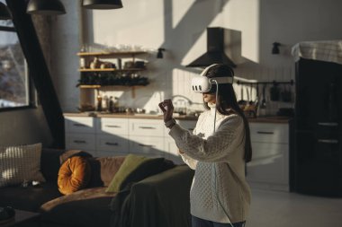 Çevrimiçi bir oyun oynarken, sevimli genç bir bayan evde VR kulaklığının keyfini çıkarıyor. Yüksek kalite fotoğraf