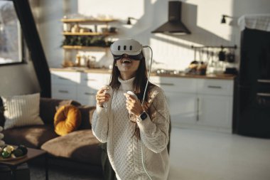 Güneş ışığı altında, enerjik genç bir kadın evde bir VR kulaklığıyla takılıyor. Yüksek kalite fotoğraf