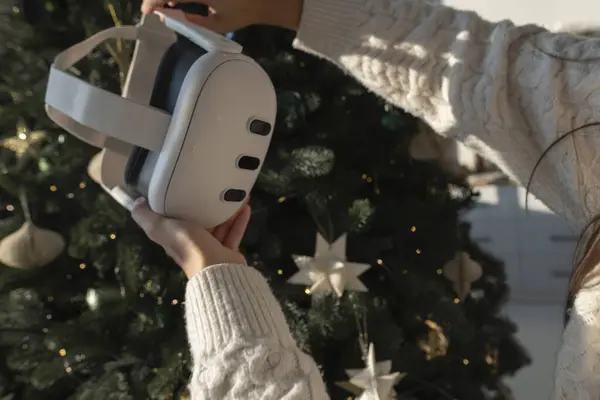 在圣诞树前 一个女孩拿着一个虚拟现实耳机 高质量的照片 免版税图库照片