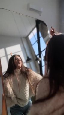 Noel geyiği maskesiyle, hayat dolu genç bir bayan aynanın önünde yansımasından zevk alıyor. Yüksek kalite 4k görüntü