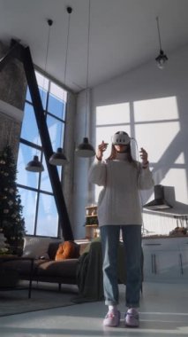 Bir Noel apartmanının güneş ışığı altında, hayat dolu genç bir kadın VR kulaklık takıyor. Yüksek kalite 4k görüntü