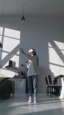 Modern, modaya uygun bir apartmanın ortasında, açık renk elbiseli genç bir kadın bir VR kulaklıkla takılıyor. Yüksek kalite 4k görüntü