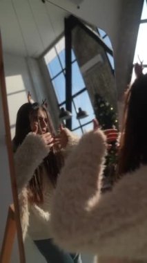 Ev aynasından önce güzel ve genç bir kız Noel geyiği maskesi deniyor. Yüksek kalite 4k görüntü