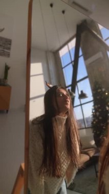 Evinin mahremiyetinde, sevimli genç bir bayan aynanın önünde bir Noel geyiği maskesi ile deney yapıyor. Yüksek kalite 4k görüntü