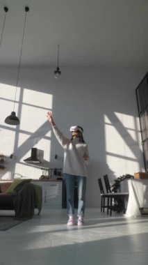 Modern bir dairede, hafif giysili, sanal gerçeklik kulaklığı takan genç bir kadın. Yüksek kalite 4k görüntü
