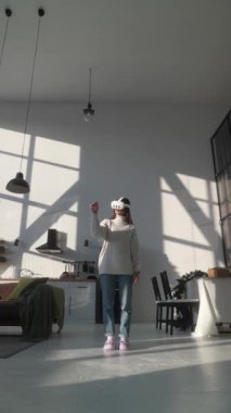 Modaya uygun, modern bir apartman ortamında genç bir kadın VR kulaklık takıyor. Yüksek kalite 4k görüntü