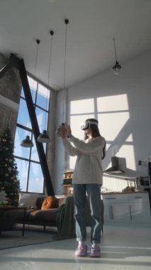 Noel ağacı arkaplanıyla, güzel genç bir kadın evde bir VR kulaklıkla takılıyor. Yüksek kalite 4k görüntü