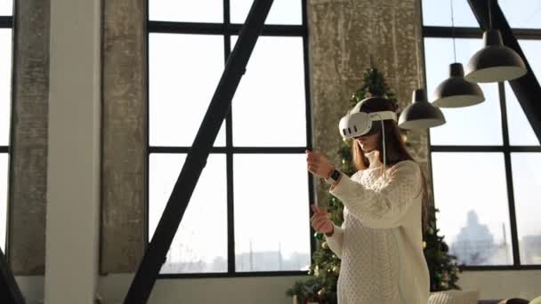 彼女の背後にあるクリスマスツリーで仮想現実のヘッドギアを寄付する楽しい若い女の子 高品質の4K映像 — ストック動画