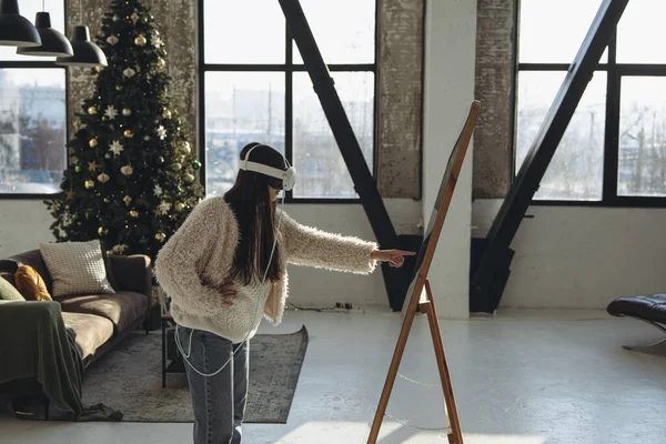 在圣诞气氛中 一位身穿浅色衣服 头戴虚拟现实耳机的年轻女士站在镜子前 高质量的照片 — 图库照片