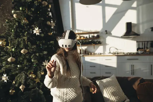 这张照片在圣诞树的背景下 在一个虚拟现实耳机中描绘了一个令人惊叹的女孩 高质量的照片 免版税图库图片