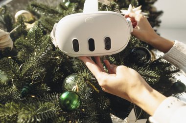 Bir Noel ağacı karşısında, bir kız elinde sanal bir gerçeklik kulaklığı tutuyor. Yüksek kalite fotoğraf