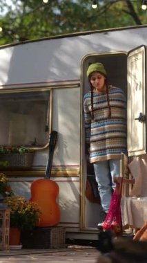 Güz bahçesindeki karavanın terasında elinde gitar ve sıcak içecek termosuyla şık genç bir hippi kız. Yüksek kalite 4k görüntü