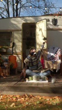 Sonbahar bahçesindeki karavanın terasında elinde gitar ve sıcak içecek termosuyla şık bir hippi kız. Yüksek kalite 4k görüntü