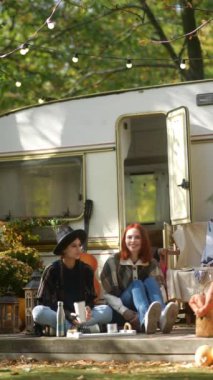 Hippi estetiğini somutlaştıran güzel genç kadınlar sonbahar parkındaki bir karavanın yanında eğleniyorlar. Yüksek kalite 4k görüntü