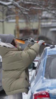 Genç bir kadın tarafından arabasından karların alınması park yerinde devam ediyor. Yüksek kalite 4k görüntü