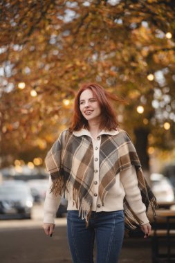 Neşeli kızıl saçlı bir kız neşe içinde gülerek sonbahar şehirlerine cazibesini katıyor. Yüksek kalite fotoğraf