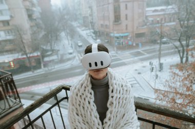 VR deneyimlerinin tadını çıkaran genç bir bayan, kış balkonunda kulaklık takıyor. Yüksek kalite fotoğraf