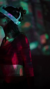 Canlı renkler projektörün üzerinde dans ederken bir kız kulaklıkla sanal gerçeklik deneyimi yaşıyor. Yüksek kalite 4k görüntü