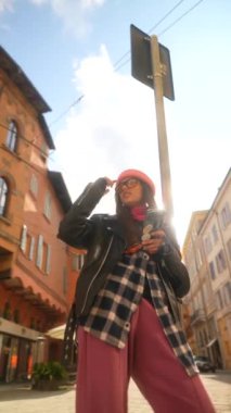Güzel bir kız, elinde telefonuyla güneşli bir İtalyan şehrinde yürümekten hoşlanır. Yüksek kalite 4k görüntü