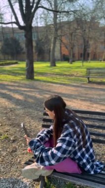 Parkta bir bankta otururken genç ve güzel bir bayan telefonda sohbet ediyor. Yüksek kalite 4k görüntü