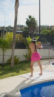 Pembe şortlu kadın havuz kenarında güneşleniyor, şapkası ve mayosuyla yaz gününün tadını çıkarıyor..