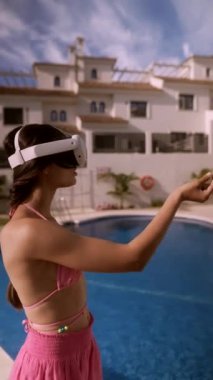 VR kulaklık takan ve pembe mayo giyen bir kadın güneşli bir tatil köyünde havuz kenarında sanal gerçeklik yaşıyor..