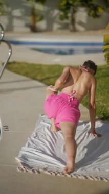 Pembe şortlu bir kadın havuz başında yoga yapıyor. Açık hava fitness ve rahatlama ile sağlığını arttırıyor.
