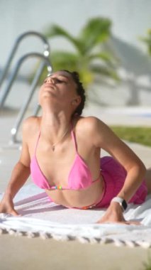 Pembe bikinili bir kadın kobra yogası yapıyor güneşli bir günde havuz başında poz veriyor, güneşlenmenin ve dinlenmenin tadını çıkarıyor.