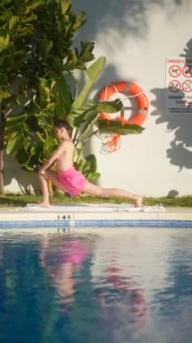 Yoga yapan bir kişi, arka planda can yeleği ve yeşillik olan bir yüzme havuzunun yanında gerinir..