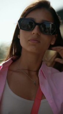 Şık bir kadın, güneşli bir günde şık kıyafetler, pembe gömlek, güneş gözlüğü ve çiçekli etekle rahat poz verir.