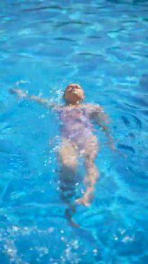 Güneşli bir yaz gününde açık mavi bir havuzda dinlenen mayo giymiş bir kadın, deniz kenarında boş vaktini somutlaştırıyor.