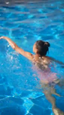 Bir kadın ferahlatıcı bir yaz gününün tadını çıkarırken berrak, mavi bir havuzda rahatça yüzüyor ve anın tadını çıkarıyor.