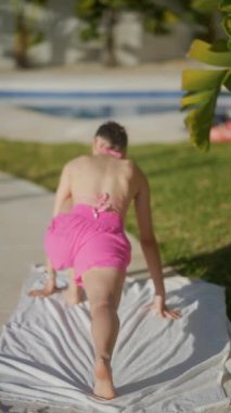 Pembe şortlu bir kadın yaz sporu için açık hava egzersizlerinin bir parçası olan yoga havuzu kenarında pratik yapıyor.