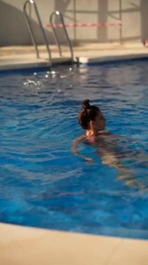 Bir kadın yaz tatili sırasında açık bir havuzda yüzerken güneşli bir günün tadını çıkarıyor.