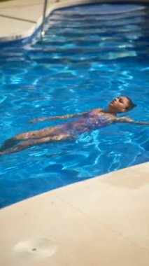 Genç bir çocuk güneşli bir günde neşeyle yüzüyor ve kristal mavi bir havuzda yüzüyor.