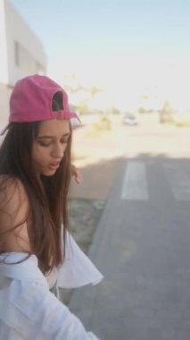 Pembe şapkalı ve günlük kıyafetli genç bir kadın güneşli bir günün tadını çıkarıyor ve etrafta dolaşıyor..