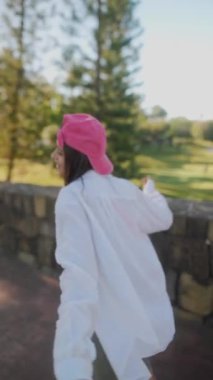 Genç bir kadın açık havada poz veriyor, günlük kıyafetlerle pembe şapkalı, rahat ve modaya uygun bir hava yaratıyor..