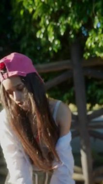 Pembe şapkalı, beyaz gömlekli ve günlük kıyafetli genç bir kadın açık havada güneşli bir günün keyfini çıkarıyor.