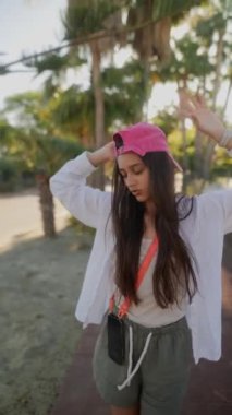 Uzun saçlı ve pembe şapkalı genç bir kadın açık havada poz veriyor, yemyeşil ve kaygısız bir ruhu somutlaştırıyor.