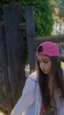 Pembe şapkalı ve günlük kıyafetli genç bir kadın güneşli bir günde enerjik bir şekilde dans eder.