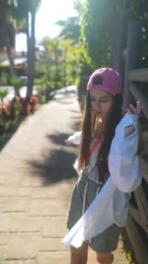 Pembe şapkalı, açık renk tişörtlü ve yeşil şortlu genç bir kız güneşli bir günün tadını çıkarıyor..