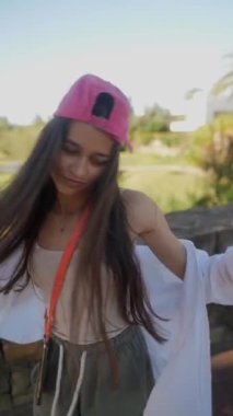 Pembe şapkalı ve günlük kıyafetli genç bir kadın güneşli bir günün tadını çıkarıyor. Parkta ve dışarıda görülebiliyor..