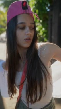 Genç bir kadın dışarıda enerjik bir şekilde dans ediyor. Pembe bir şapka takıyor ve gündelik kıyafetler giyiyor. Anın tadını çıkarıyor..