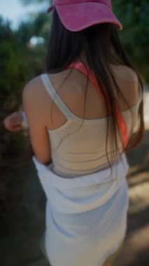 Genç bir kadın sıradan giyinmiş, pembe bir şapka takıyor, güneşli bir günün tadını çıkarıyor, yürüyor ve vurucu pozlar veriyor.