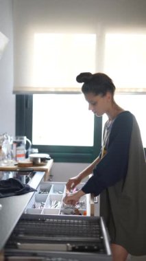 Gündüz vakti modern, aydınlık bir mutfakta mutfak aletleri düzenleyen bir kadın, organizasyona odaklanıyor.