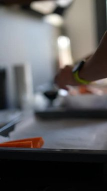 Mutfakta bir insan havuç doğruyor, yeşil akıllı bacaklara bakıyor, yemek aletleri ve taze malzemeler arasında.