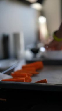 Eller, çağdaş bir mutfak ortamında fırın tepsisine taze havuç dilimleri koyuyor.