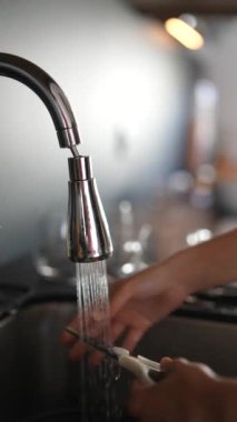 Modern bir lavaboda akan suyun altında mutfak bıçağını temizlemek, gıda hazırlığında hijyen ve güvenliği sağlamak.